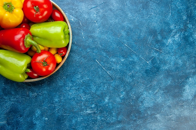 Ver la mitad superior de verduras tomates cherry pimientos tomates de diferentes colores en un tazón en la mesa azul con lugar libre