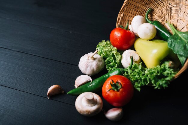 Verduras crudas frescas con la cesta de mimbre en fondo de madera negro