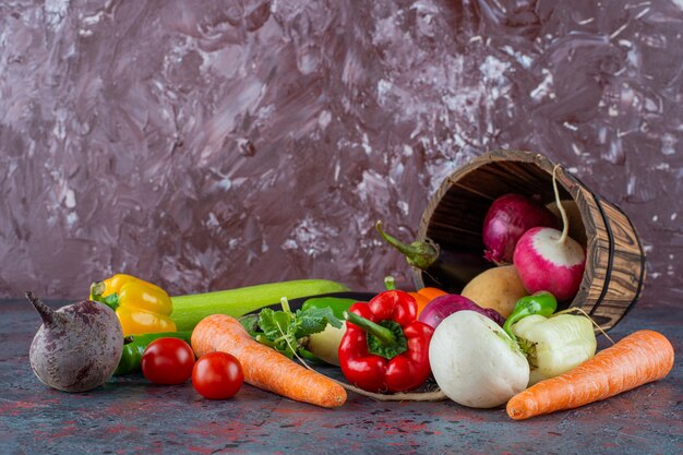 Verduras en el cubo volcado, sobre el fondo de mármol.