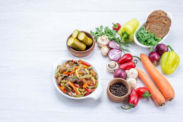 Verduras frescas como pimiento, zanahoria, cebolla con hogazas de pan y plato de carne en rodajas en el escritorio blanco, comida vegetal vitamina