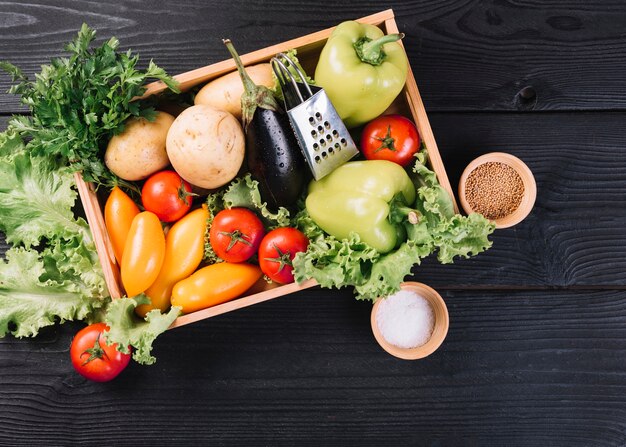 Verduras frescas en envase y especias sobre fondo de madera negro