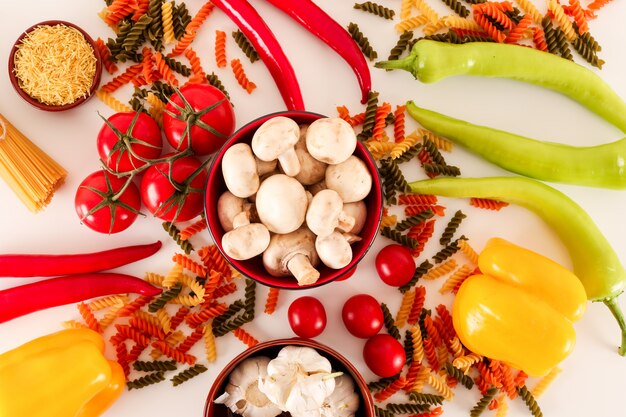 verduras frescas y pasta colorida con champiñones ajo pimienta sobre superficie blanca