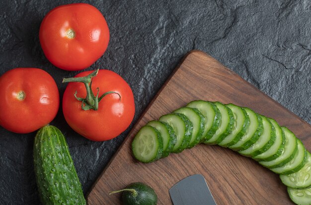 Verduras frescas en rodajas sobre una mesa negra mojada. Rodajas de tomate y pepino sobre tabla de madera. Foto de alta calidad