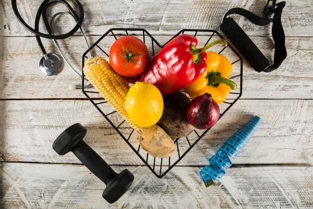 Verduras frescas rodeadas de equipos de fitness; estetoscopio y cinta métrica