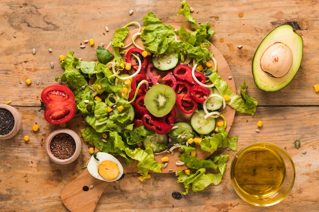 Foto gratuita verduras y frutas picadas en la tabla de cortar con ingredientes; huevo cocido y aceite sobre fondo de madera.