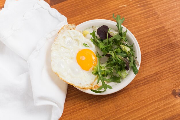 Verduras de hoja y medio huevos fritos en un plato sobre el escritorio de madera