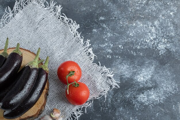 Verduras orgánicas frescas. Berenjenas moradas sobre plancha de madera con tomate y ajo