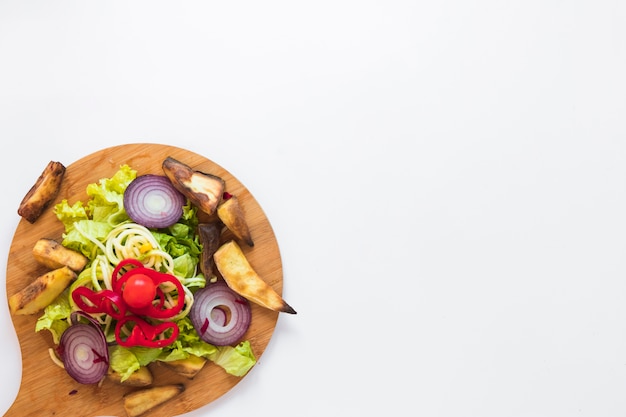 Verduras picadas y patata asada en tabla de cortar de madera sobre fondo blanco