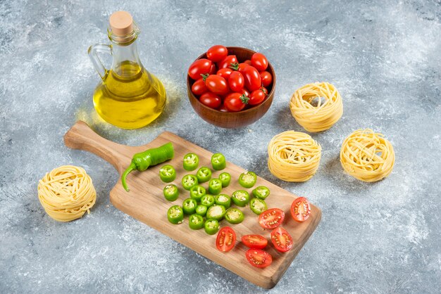 Verduras en rodajas, aceite de oliva y nidos de pasta sobre fondo de mármol.