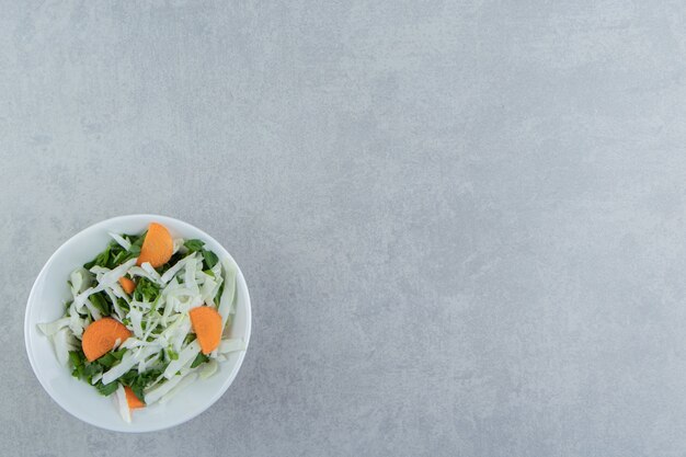 Verduras en rodajas sabrosas en un cuenco, sobre el fondo de mármol.