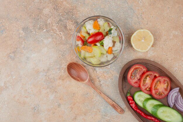 Verduras sabrosas en placa de vidrio con tablero de madera de tomate, pepino y cebolla en mármol