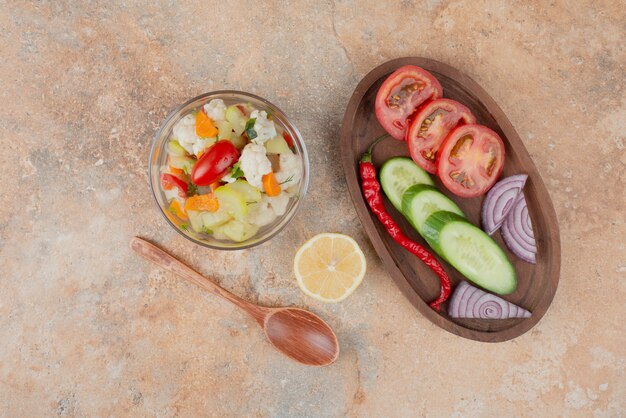 Verduras sabrosas en placa de vidrio con tablero de madera de tomate, pepino y cebolla sobre superficie de mármol