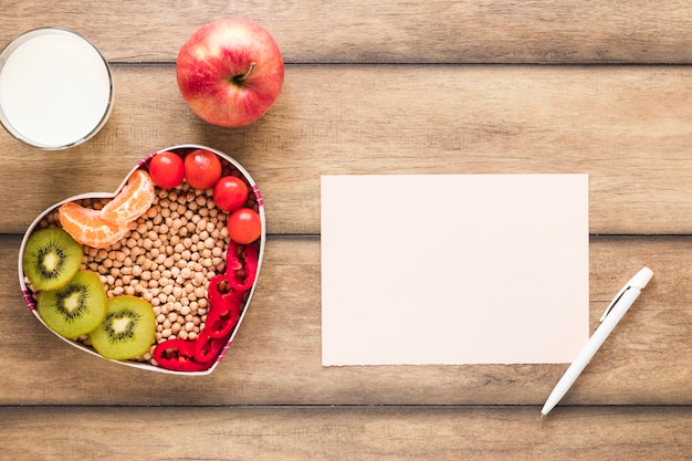 Foto gratuita verduras saludables; frutas leche con papel en blanco y pluma en mesa de madera