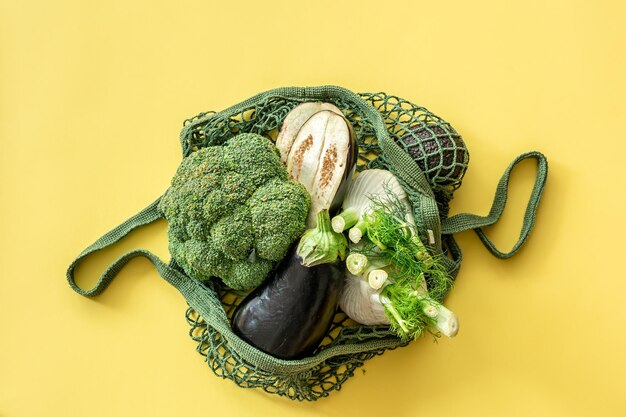 Verduras verdes frescas en una bolsa de hilo verde sobre un fondo amarillo plano