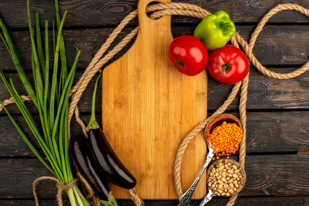 Verduras una vista superior de verduras maduras como tomates rojos, berenjenas y pimientos verdes junto con frijoles y verduras en un escritorio de madera rústica