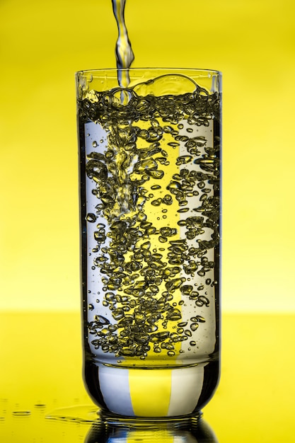 Verter agua en vidrio sobre pared amarilla