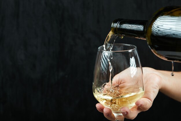 Verter vino blanco en la copa de vino sobre una superficie oscura