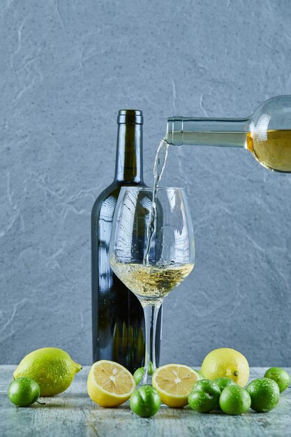 Verter vino blanco en el vaso y limones, botella de vino y ciruelas de cereza a un lado