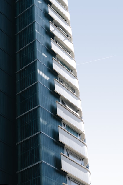 Vertical de un edificio de cristal con balcones blancos bajo el cielo azul