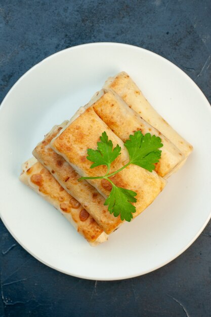 Vertical de envolturas de lavash frito en un plato servido con verde sobre fondo oscuro