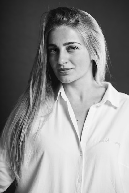 Vertical en escala de grises retrato de una atractiva mujer rubia caucásica con una camisa blanca posando