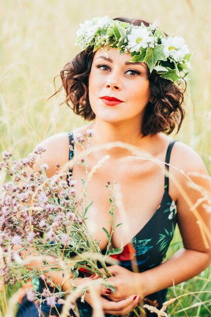 Vertical de la mujer caucásica con una corona de flores recogiendo flores en el campo