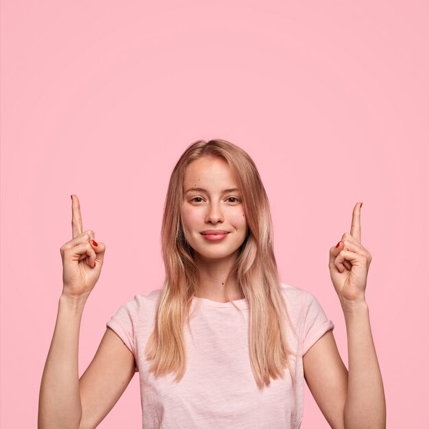 Vertical retrato de mujer joven feliz tiene cabello largo, puntos con dos dedos en la parte superior