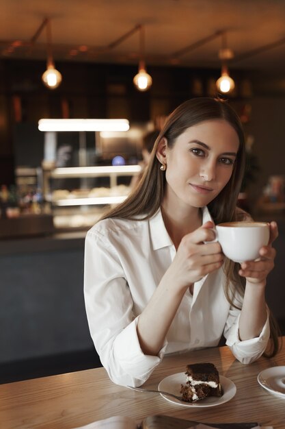 Vertical retrato de mujer joven femenina romántica tomando café solo en la acogedora cafetería.