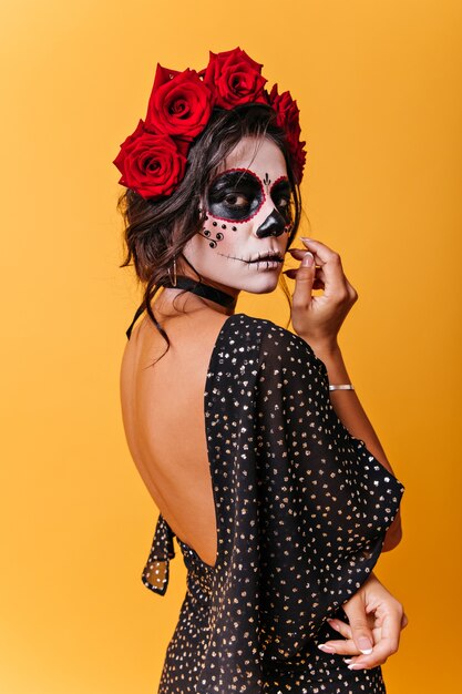 Vertical retrato de mujer mexicana con rosas en la cabeza. Chica con máscara de carnaval posando pensativamente