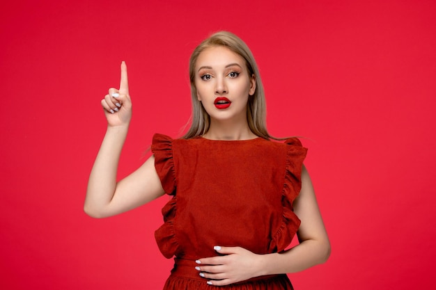 Vestido rojo linda chica elegante con clase en vestido burdeos con lápiz labial rojo sorprendido con el dedo hacia arriba