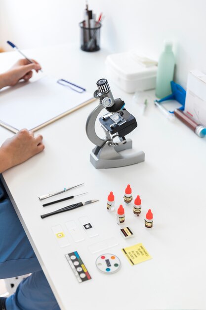 Veterinario escribiendo en el portapapeles con microscopio y equipos médicos en el escritorio del laboratorio