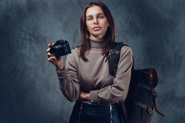 Una viajera morena con mochila tiene una cámara fotográfica compacta.