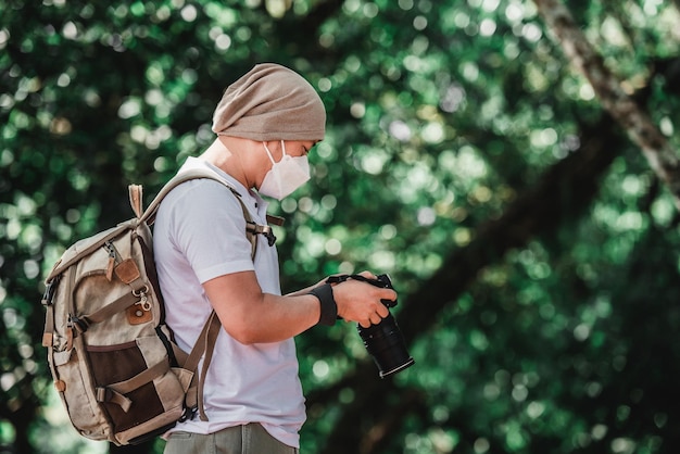 Foto gratuita el viajero asiático usa una máscara médica con mochila revisando una foto en la cámara en el parque con espacio para copiar fotógrafo de viajes concepto de vocación y vacaciones