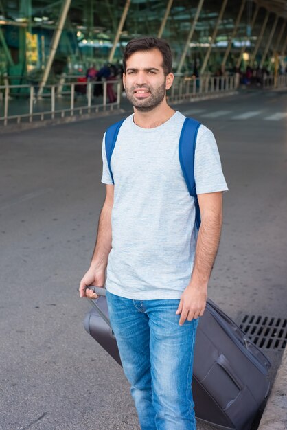 Viajero cansado caminando con maleta cerca del aeropuerto