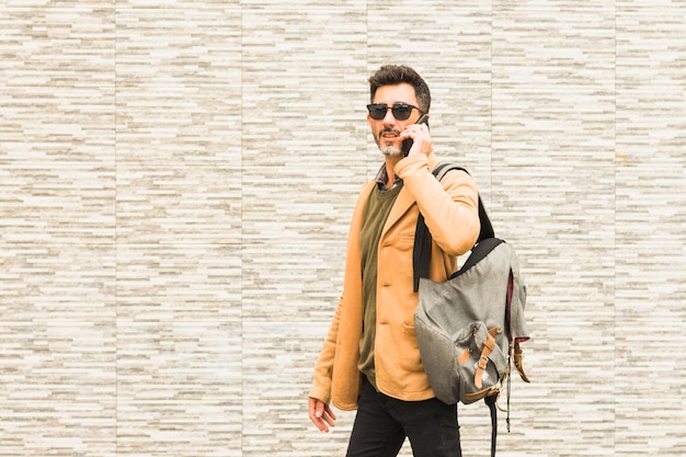 Viajero elegante de pie contra la pared hablando por teléfono móvil