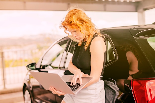 Foto gratuita viajero femenino con la computadora portátil que se coloca al lado del coche