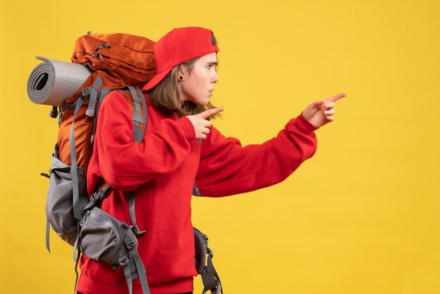 Viajero femenino fresco vista frontal con mochila apuntando con los dedos a la derecha
