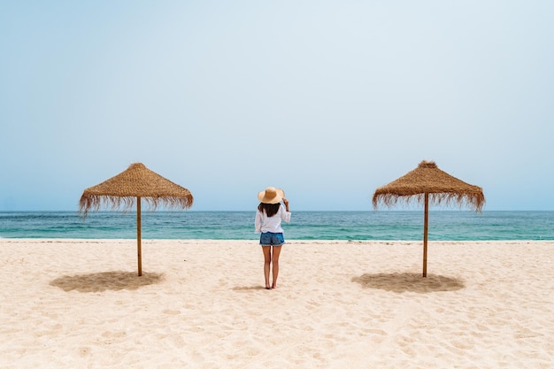 Foto gratuita viajero femenino de pie sobre la arena cerca del océano