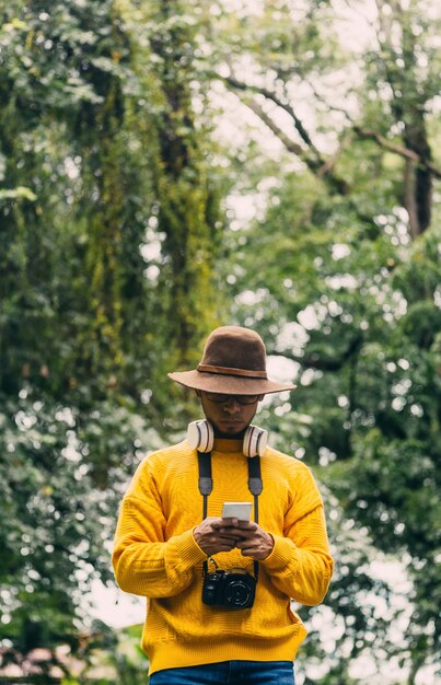 Viajero joven en un bosque verde, comprobando su teléfono móvil.