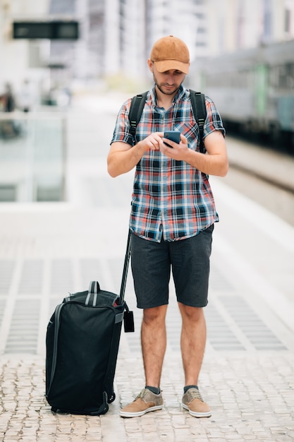 Viajero joven en la estación de ferrocarril con teléfono en la estación de tren