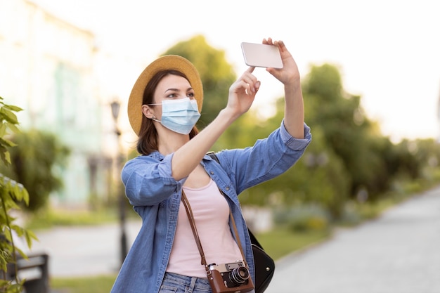 Foto gratuita viajero con mascarilla y sombrero tomando fotos