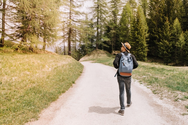 Viajero masculino con mochila azul grande que va a la espesura del bosque y mira a su alrededor con interés