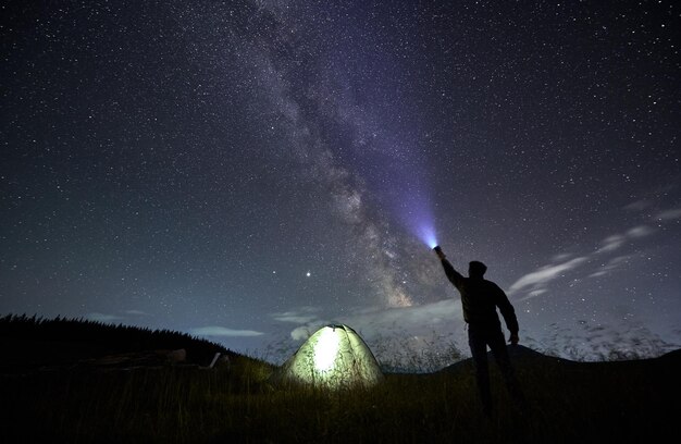 Viajero masculino que brilla con una linterna en el cielo estrellado de la noche