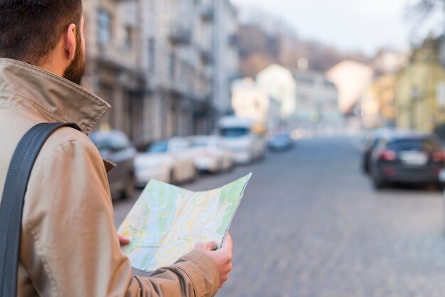 Un viajero masculino que sostiene el mapa en la mano encontrando el camino en la calle de la ciudad