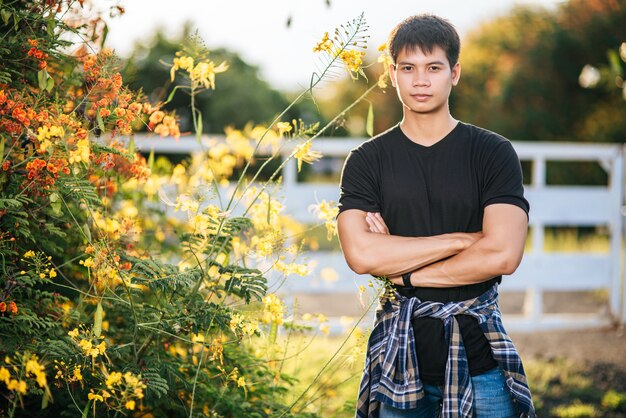 El viajero masculino viste una camisa negra y se para en un jardín de flores.