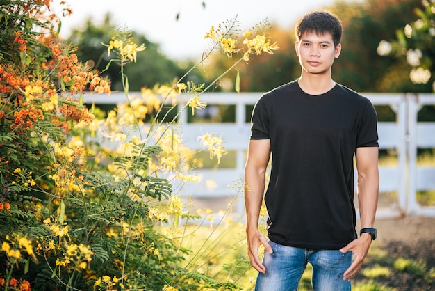 El viajero masculino viste una camisa negra y se para en un jardín de flores.