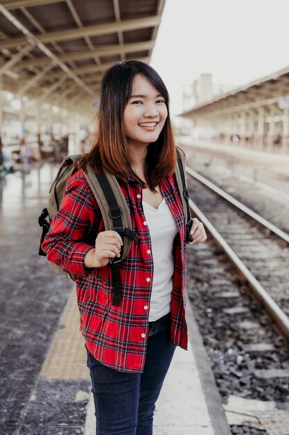 Viajero mochilero joven asiática caminando solo en la plataforma de la estación de tren con mochila