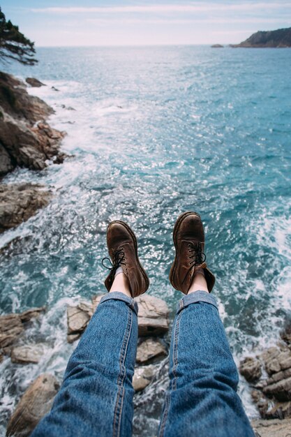 Viajero mujer en jeans azul y botas de cuero marrón grueso para aventuras de senderismo se sienta en el borde del acantilado