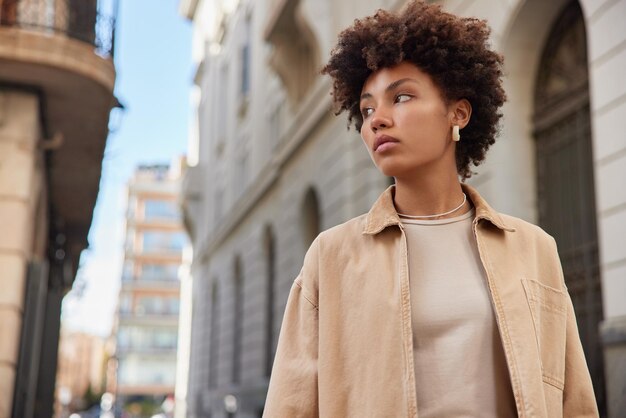 Viajero serio reflexivo va de turismo en la ciudad concentrada lejos viste chaqueta beige piensa en algo durante el día contra el fondo borroso. Personas que viajan y estilo de vida.