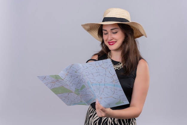 Viajero sonriente joven vestida con camiseta negra con sombrero sosteniendo un mapa sobre fondo blanco.